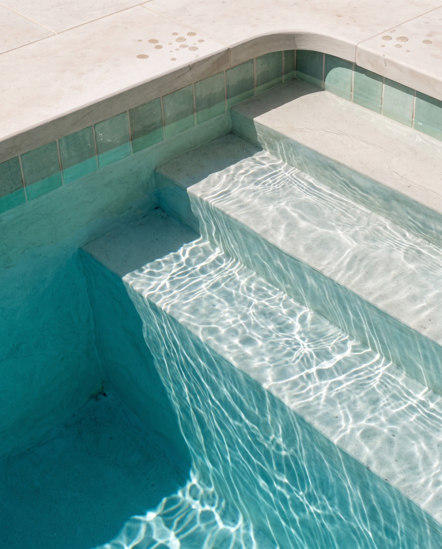 Concept visualization: sunlight rippling across submerged pool steps below a band of sea-green waterline tile